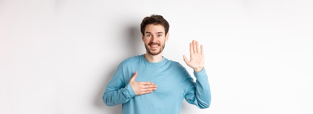 Foto grátis homem sorridente levantando o braço e segurando a mão no coração fazendo promessa dizer a verdade jurar ou fazer juramento s