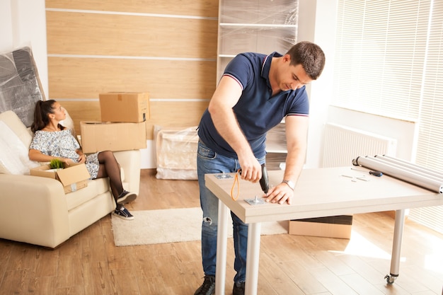 Homem sorridente montando móveis de auto-montagem na nova casa. móveis em casa nova.