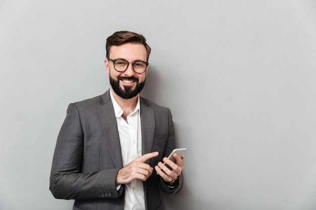 Homem sorridente na camisa branca, digitando a mensagem de texto ou rolagem de feed na rede social usando o smartphone sobre cinza
