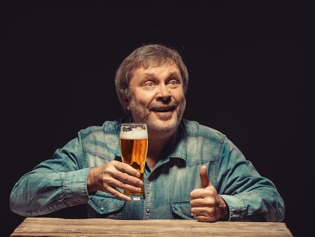 Homem sorridente na camisa jeans com copo de cerveja