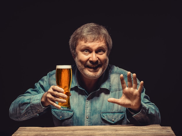 Homem sorridente na camisa jeans com copo de cerveja