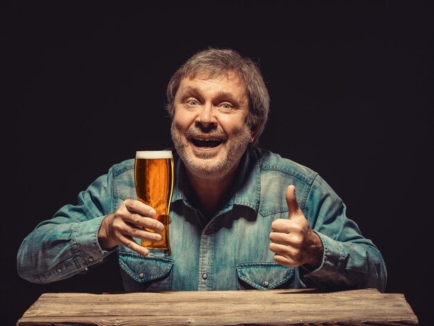 homem sorridente na camisa jeans com copo de cerveja