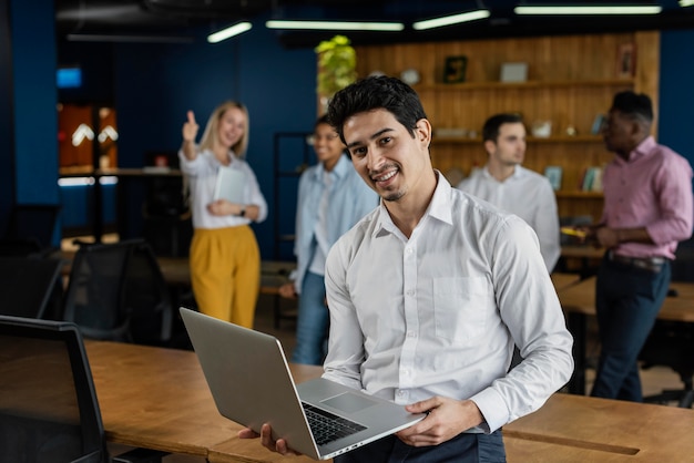 Homem sorridente no trabalho, segurando um laptop e posando