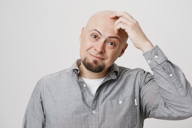 Foto grátis homem sorridente perplexo coçando a cabeça careca pensativo