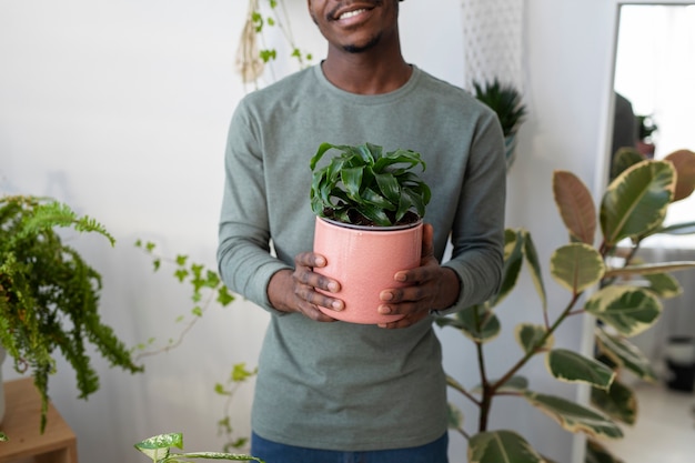 Foto grátis homem sorridente segurando planta em casa vista frontal