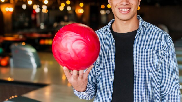 Homem sorridente segurando uma bola de boliche vermelha