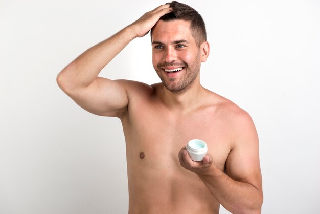 Homem sorridente sem camisa, aplicando cera no cabelo dele contra o pano de fundo branco