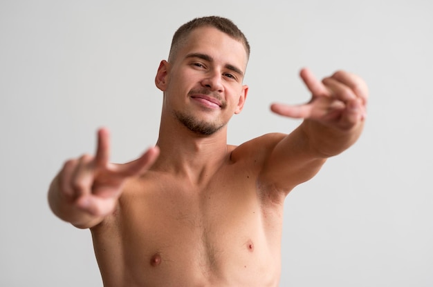 Homem sorridente sem camisa posando enquanto faz os sinais da paz