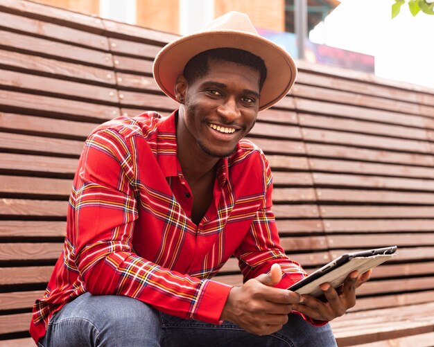 Homem sorridente sentado em um banco segurando um tablet digital