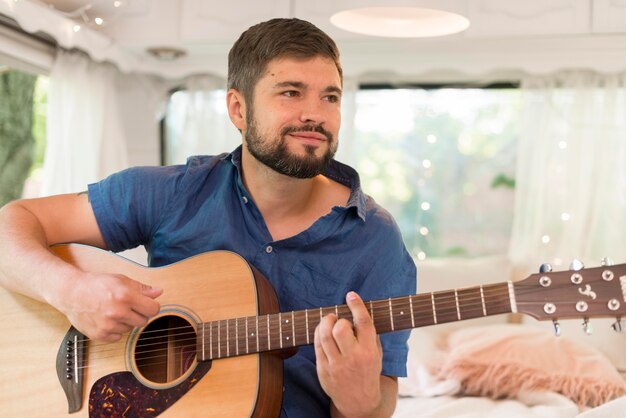 Homem sorridente tocando violão em sua caravana