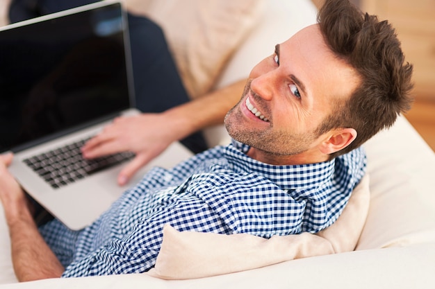 Homem sorridente usando computador na sala de estar