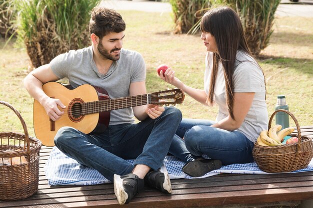 Homem sorridente, violão jogo, com, seu, namorada, segurando, maçã vermelha, em, mão