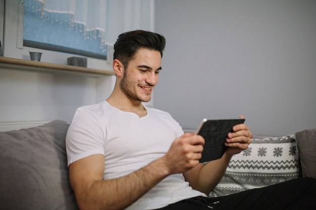 Homem sorrindo com tablet no sofá