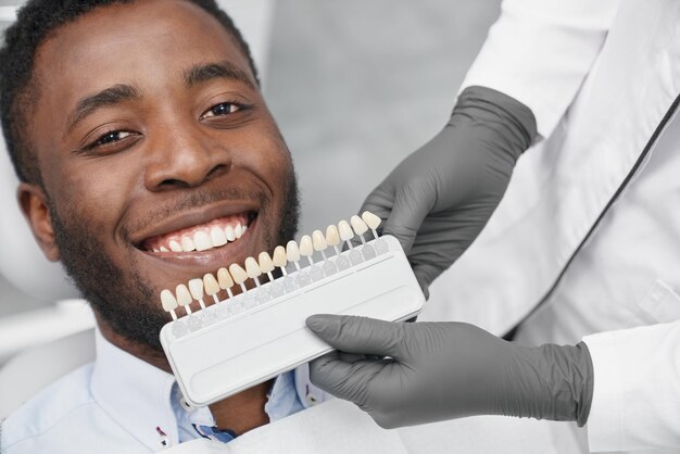 Homem sorrindo enquanto dentista feminina mantendo gama de obturações