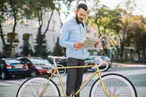 Foto grátis homem sorrindo lendo jornal perto da bicicleta