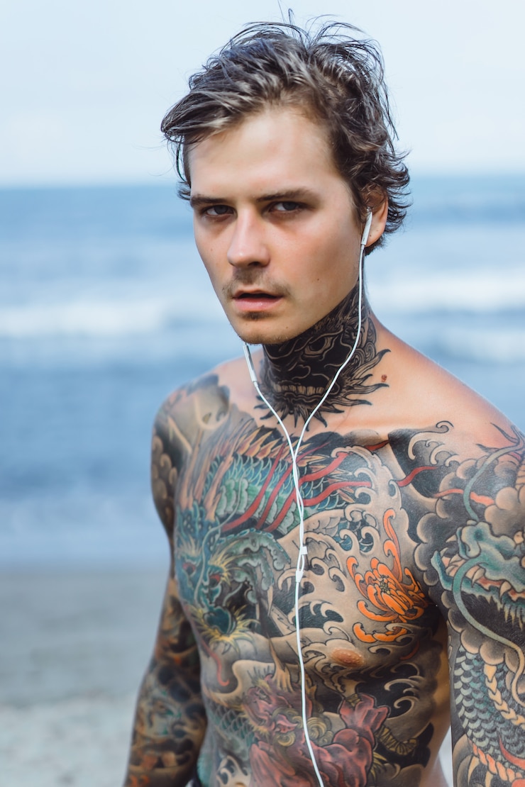 Foto grátis homem tatuado com fones de ouvido contra o céu azul no oceano