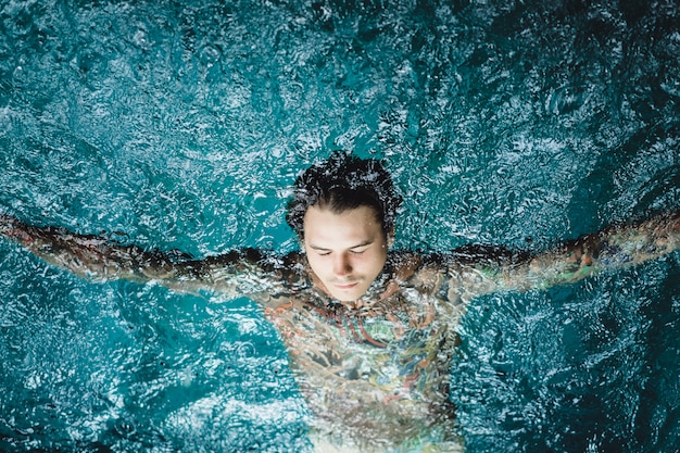 Foto grátis homem tatuado na piscina na chuva.