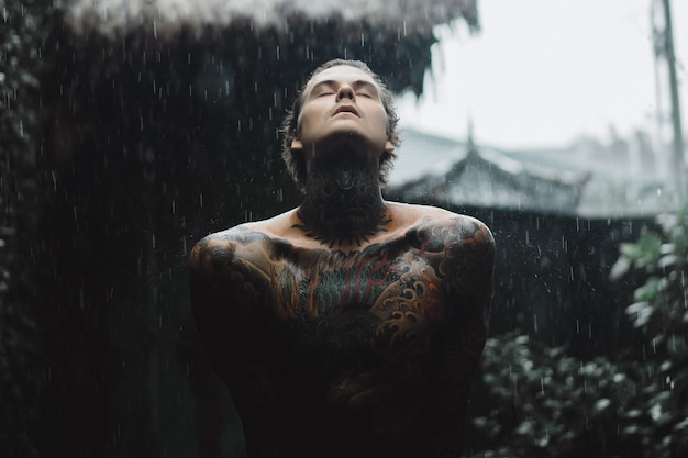 Homem tatuado posando na chuva