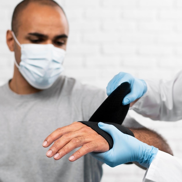 Homem tendo o pulso enfaixado por fisioterapeuta