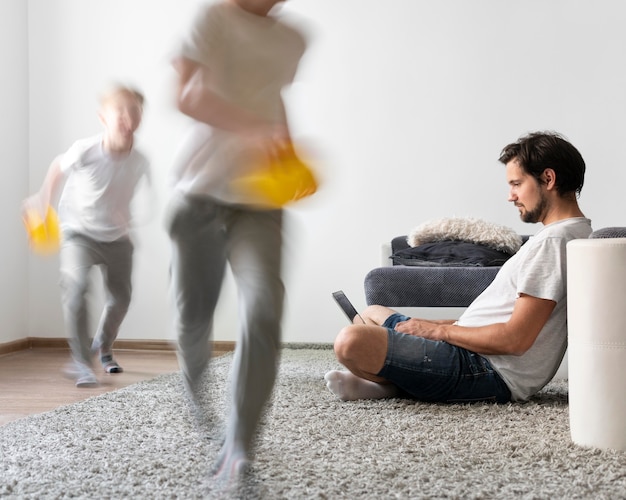 Foto grátis homem tentando trabalhar em um laptop de casa enquanto os filhos dela estão correndo