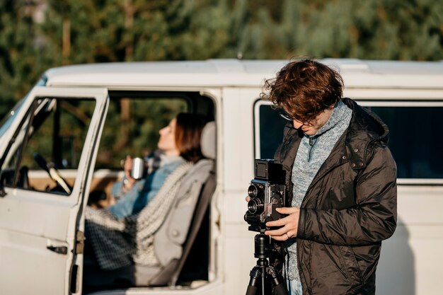 Homem tirando foto com uma câmera retrô ao lado de sua van