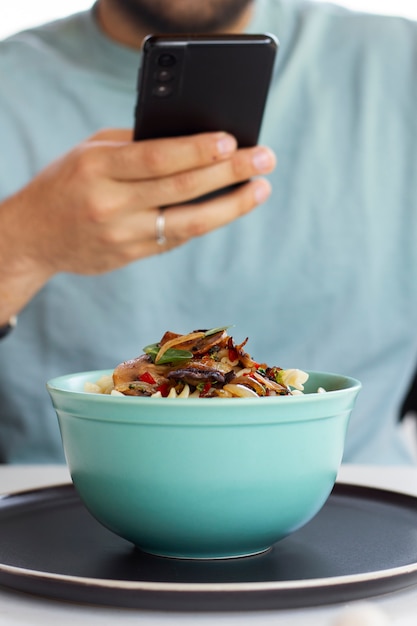 Homem tirando foto de tigela de macarrão com smartphone