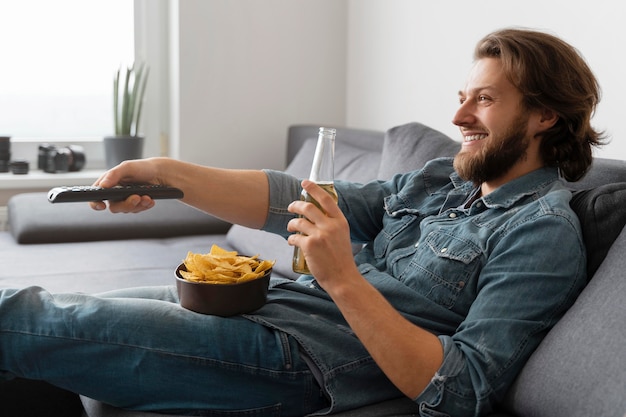 Foto grátis homem tiro médio com bebida assistindo tv