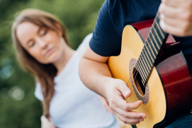 Homem tocando guitarra com mulher no fundo desfocado