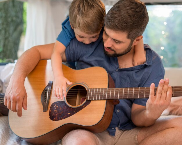 Homem tocando violão em um trailer ao lado de seu filho