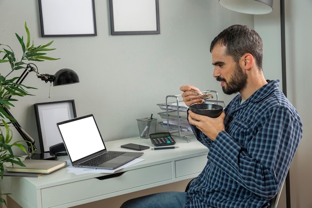 Homem tomando café da manhã enquanto trabalha em casa