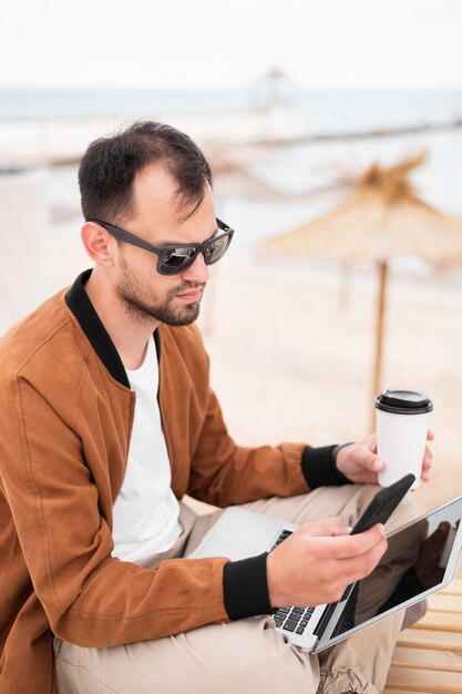 Homem tomando café na praia e trabalhando no laptop