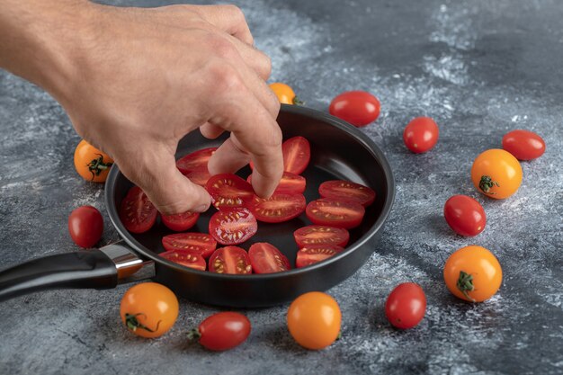 Homem tomando meio corte o tomate cereja da frigideira.