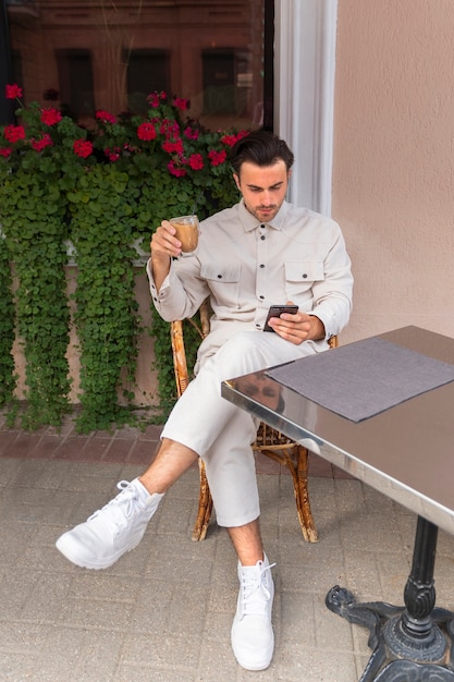 Homem tomando um café gelado enquanto estiver usando smartphone