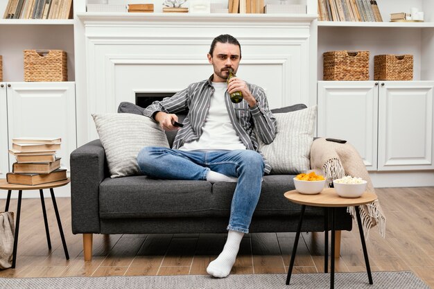 Homem tomando uma cerveja e assistindo tv sentado no sofá