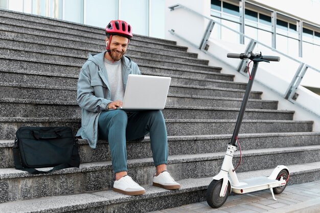 Homem trabalhando em seu laptop ao lado de sua scooter