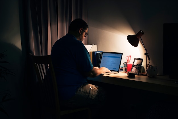 Homem trabalhando em um escritório doméstico escuro com um laptop