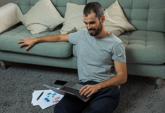Homem trabalhando em um laptop ao lado do sofá