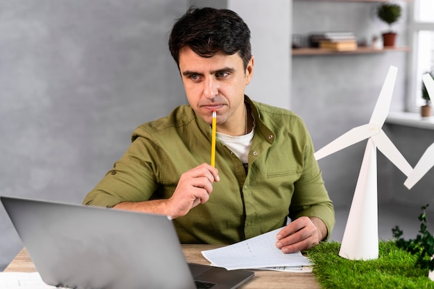 Homem trabalhando em um projeto de energia eólica ecologicamente correto e pensando enquanto segura um lápis