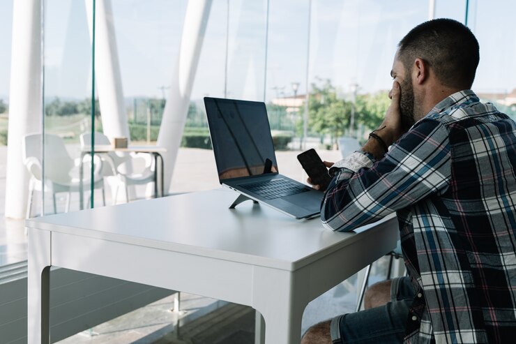 Homem trabalhando na frente do laptop e com um celular na mão em um espaço de trabalho