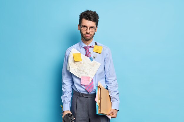 Homem triste com a barba por fazer olha seriamente para a câmera segurando café e papéis cansado de preparar relatório vestido com roupas formais chega para reunião de negócios