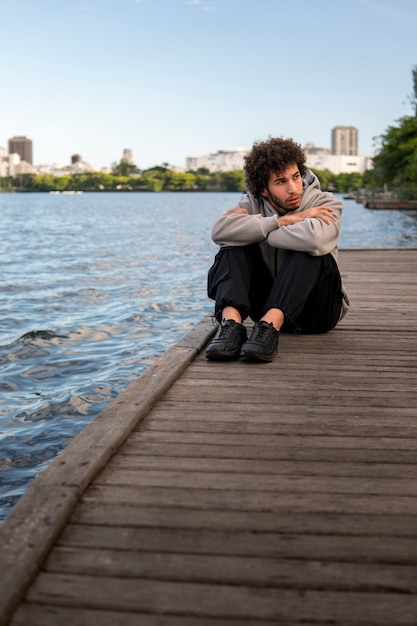 Foto grátis homem triste e contemplativo sentado à beira do lago