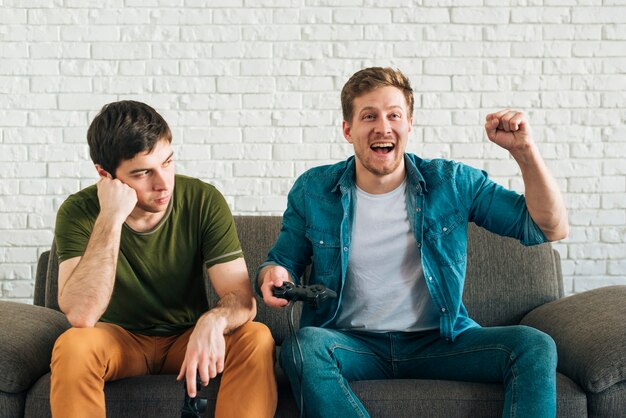 Homem triste olhando feliz amigo torcendo depois de ganhar o videogame