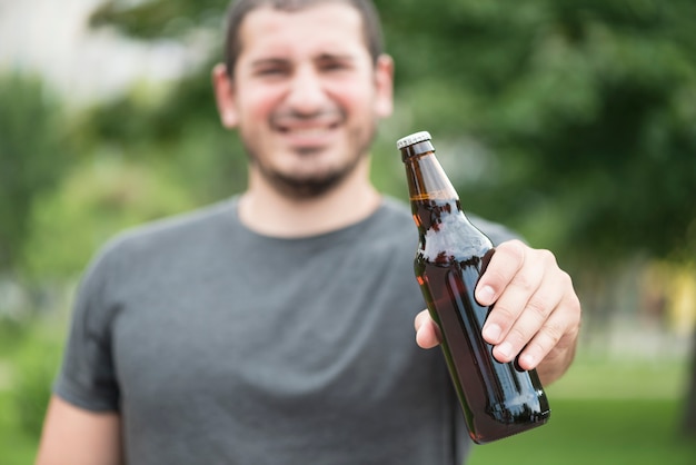 Homem turva, mostrando a garrafa de cerveja no parque