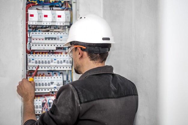 Homem, um técnico elétrico trabalhando em um painel de distribuição com fusíveis. Instalação e conexão de equipamentos elétricos.