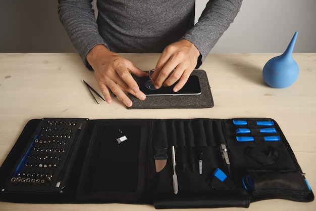 Homem usa plug a vácuo para remover a tela do telefone quebrado, seu kit de ferramentas com ferramentas especiais perto