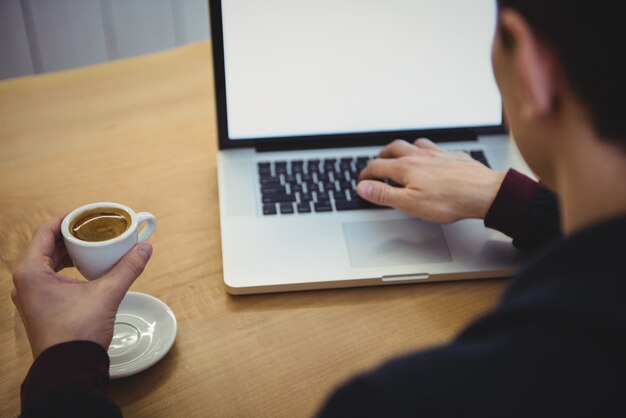 Homem usando laptop enquanto toma café