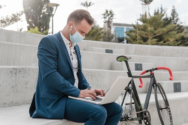 Homem usando máscara médica sentado ao lado de sua bicicleta