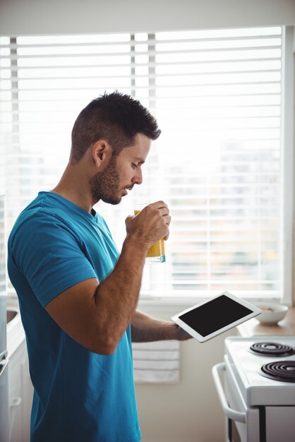 Homem usando seu tablet digital enquanto toma um copo de suco