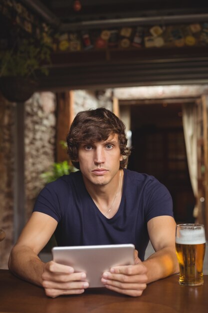 Homem usando tablet digital com copo de cerveja na mesa