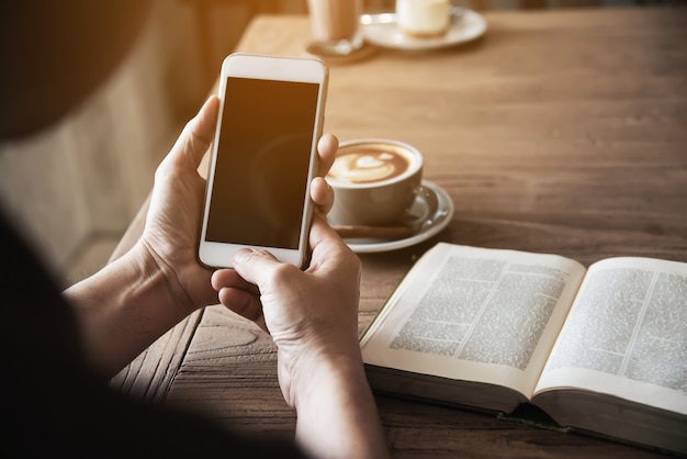 Homem, usando, telefone móvel, bebendo um café, e, lendo um livro